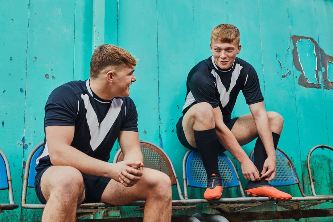 Two young male rugby players sitting in from of an aqua wall