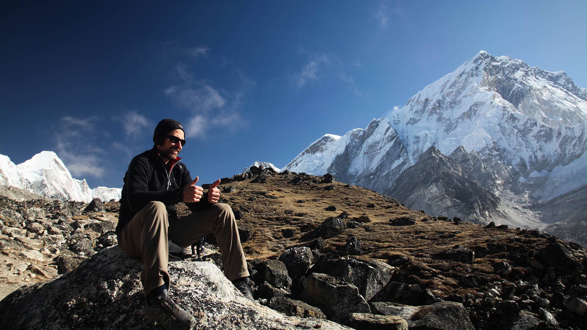 Photo of climnber on sitting on a rock at Everest Base Camp giving a thumbs up while thinkig about raising funds for Movember