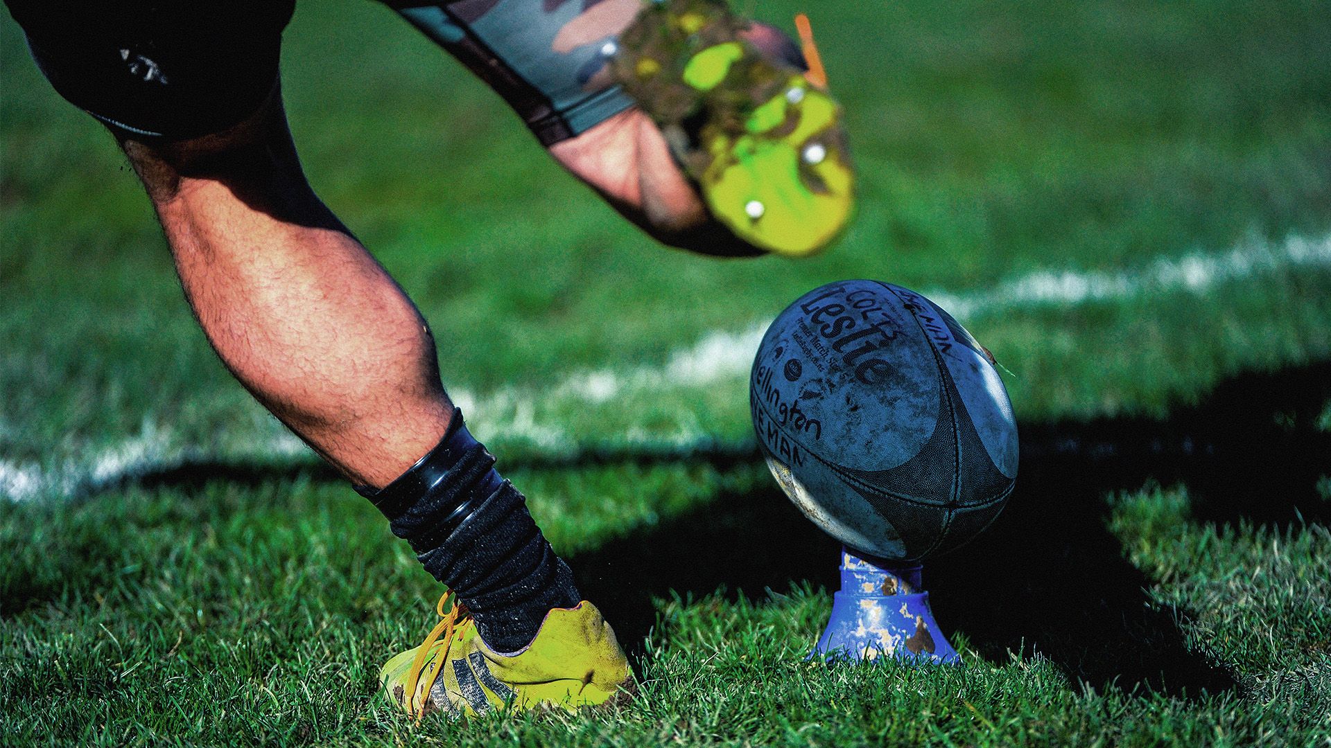 Mans foot kicking positioned to kick a rugby ball on a field.
