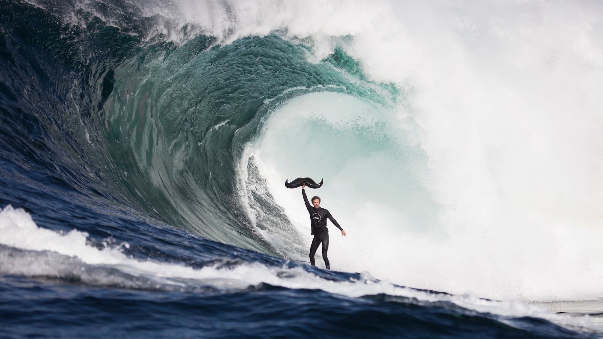 Movember moustache logo held by surfer in a wave