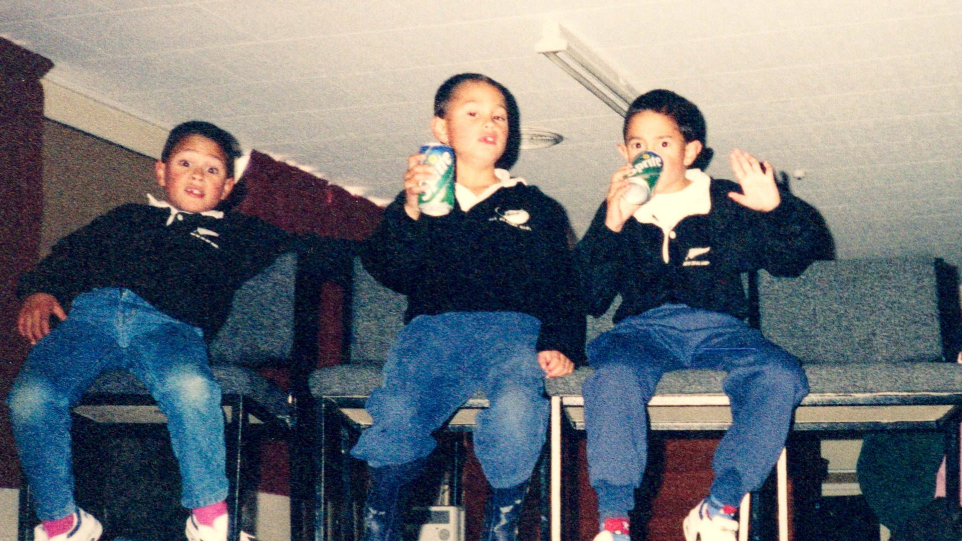 Old photo of three boys sit in all blacks jerseys drinking can of sprite