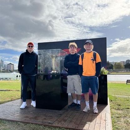 Photo of three young men posing beside what appears to be an outdoors sculpture.