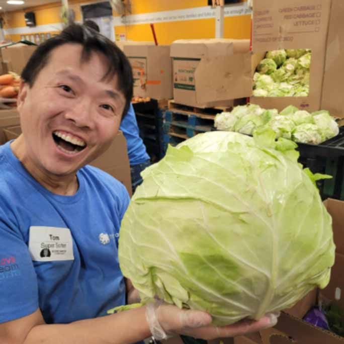 Photo of a delighted man, holding an enormous cabbage to camera.