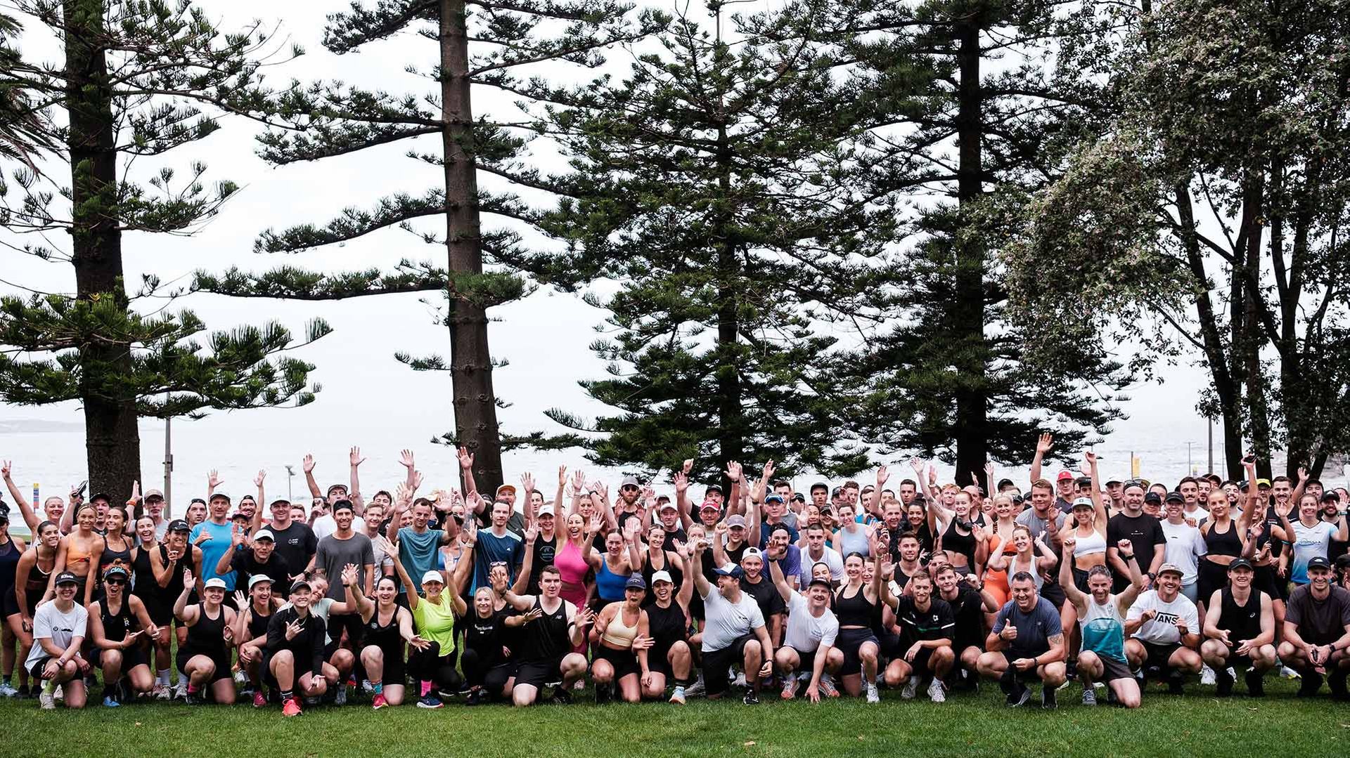 Photo of a cross-country running team assembled in a forest and waving to camera.