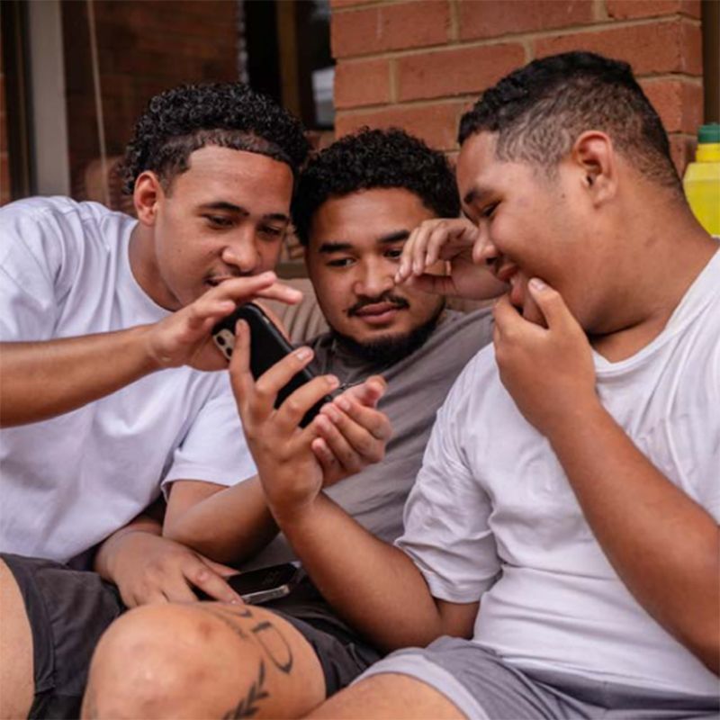 Photo of three seated young men looking at a phone screen