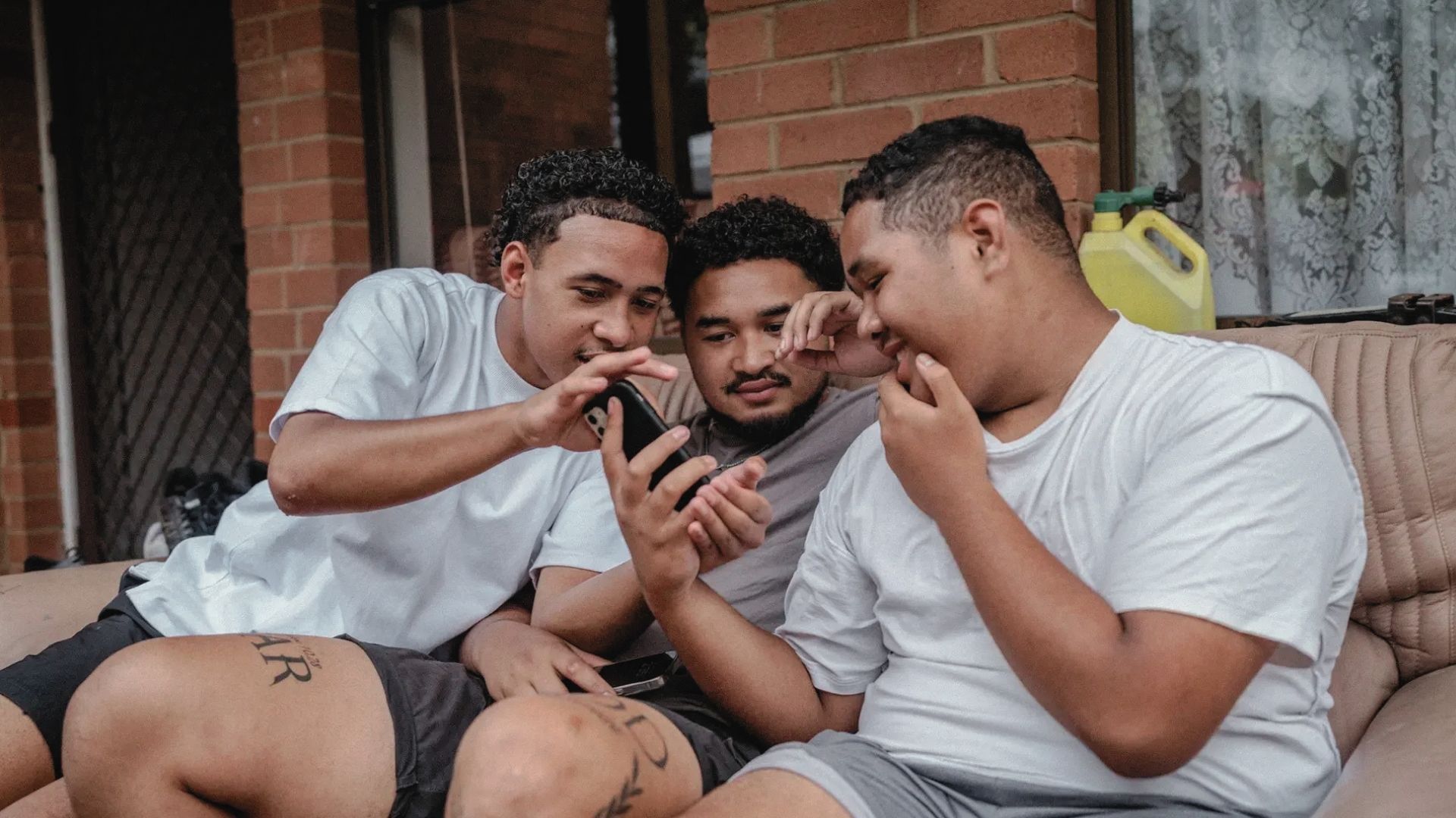 Three young men huddled around a phone screen looking entertained by something on the phone.