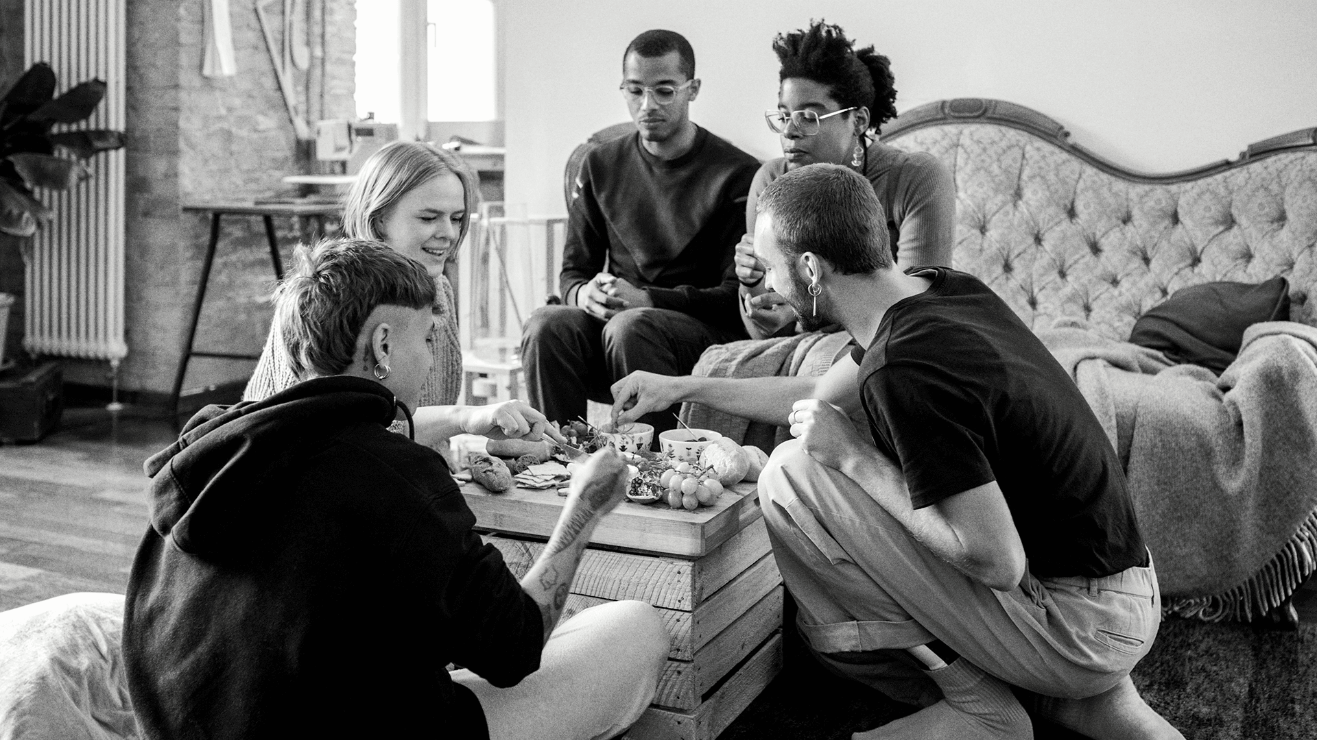 A group of friends gathered around a cheese board in a home.