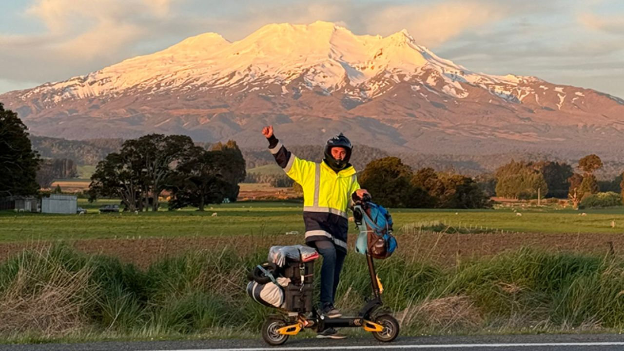 Tane Tarlton poses in front of a mountain on his electric scooter 