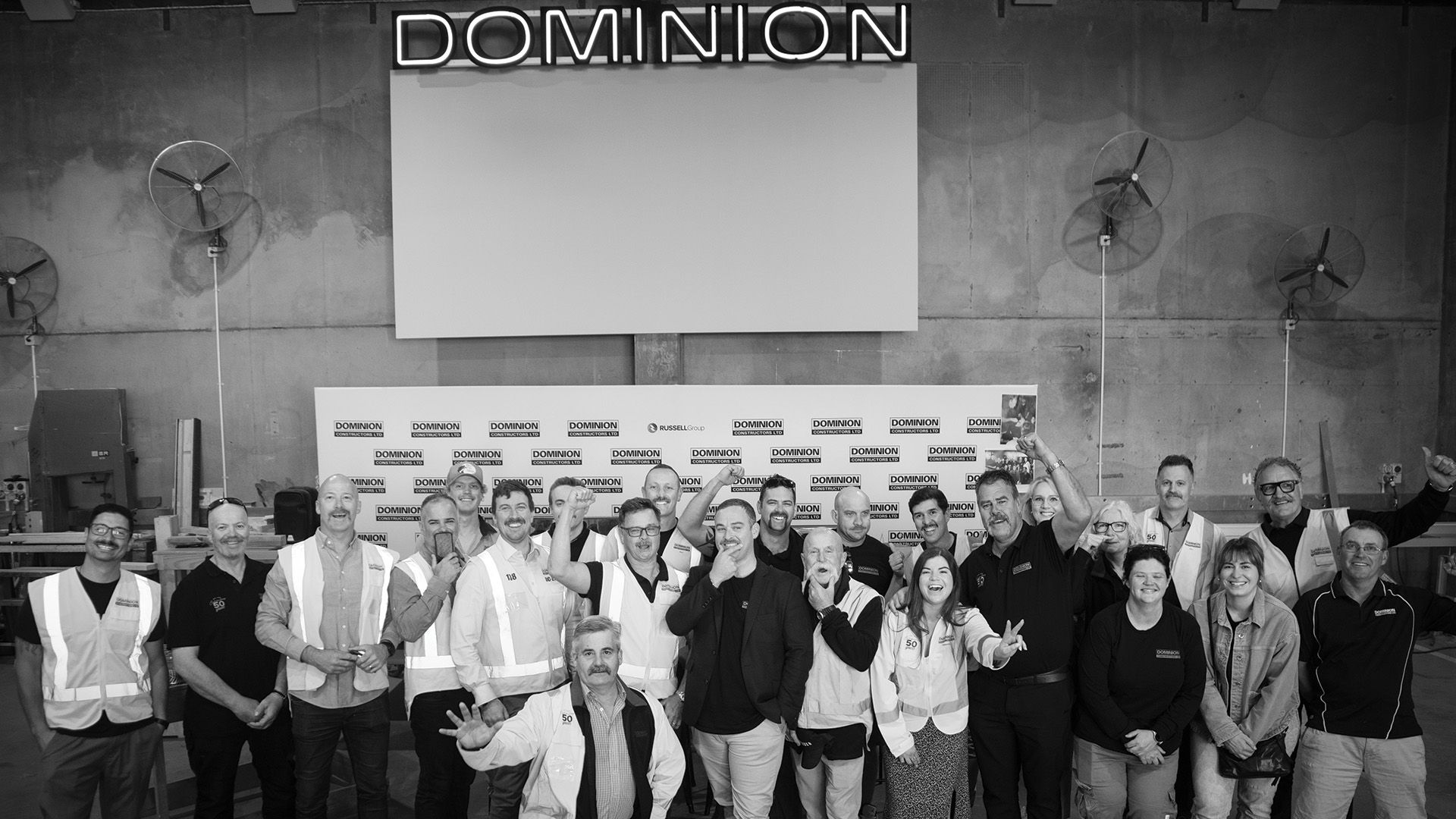 Black and white, team of construction workers pose in front of media wall at fundraising event