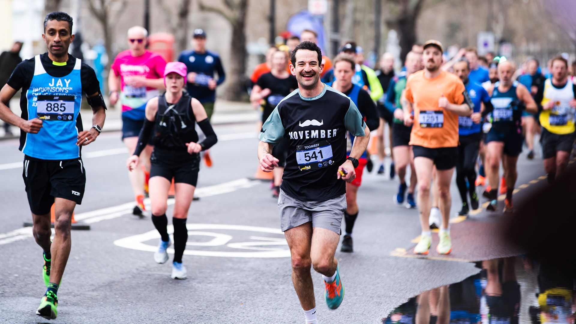 Photo of a man wearing Movember-branded running gear, running to camera as part of a running crowe.