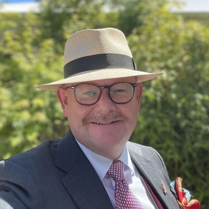 Photo of a dapper man with a marvellous moustache, smiling to camera.