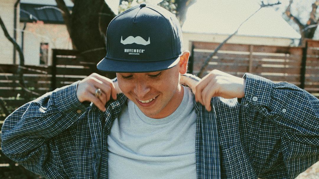 Smiling young man wearing a Movember cap.