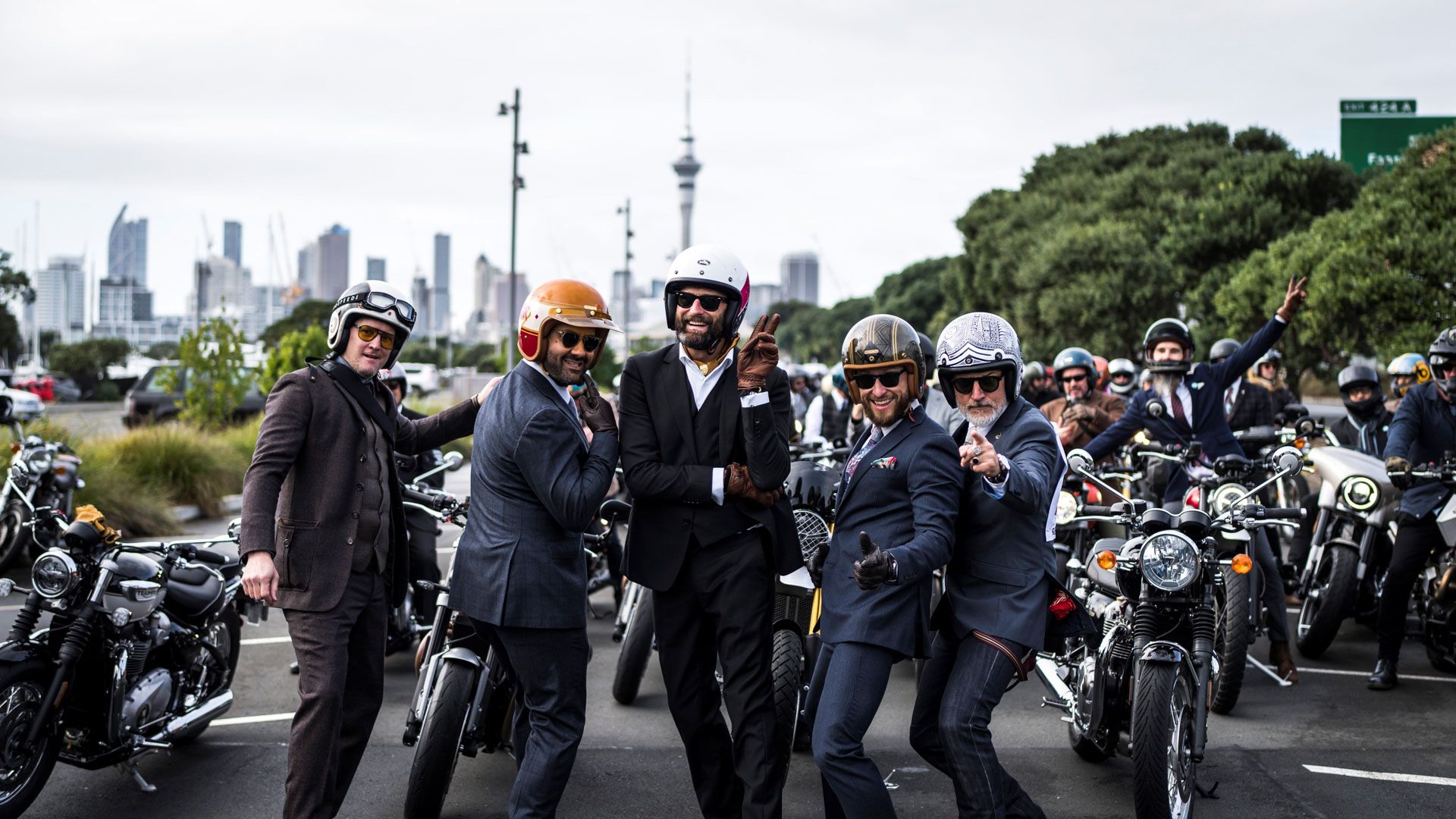Five men in suits stand on road in front a motorbikes with Auckland skyline in the background including the sky tower