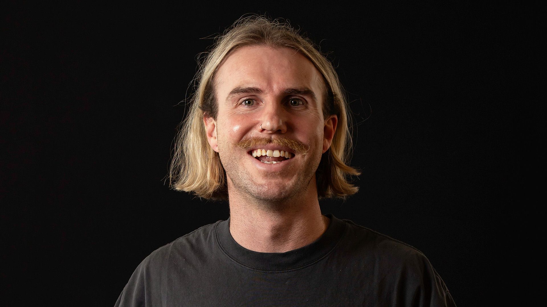 Portrait of man with long hair smiles at camera with black tshirt and background