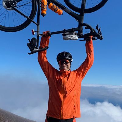 Man triumphantly holding aloft his bicycle. Clouds are visible in the background.